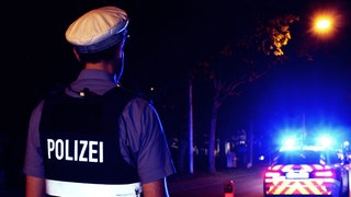 Ein Polizist steht im Dunkeln vor einem Polizeiauto.