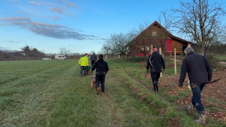 Eine Gruppe von Menschen läuft mit Schubkarren und Schaufeln zu einem Haus. Sie haben bei der Aktion "Baumstark für alle" auf dem Hofgut Serrig geholfen.