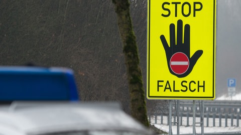 Schild an einer Autobahnauffahrt, das vor Auffahrt in falscher Fahrtrichtung warnt, daneben ein Polizeiauto.