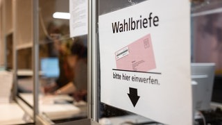 Ein Schild weist in einem Wahlbüro auf eine Wahlurne hin.