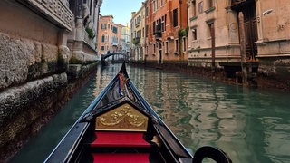 Eine Gondel die in einem engen venezianischen Kanal, umgeben von historischen Gebäuden, auf eine kleine Brücke zugleitet. 
