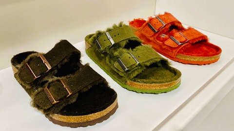 Auf weißem Grund präsentierte Birkenstock-Modelle mit Kunstfell-Besatz in Schwarz, Grün und Orange. Marktcheck checkt Schuhe von Birkenstock auf Qualität, Preis und Image: Ist der Hype gerechtfertigt? Wie bequem und gesund sind die Latschen wirklich? Lohnen sich Birkenstocks?