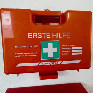Ein roter Erste-Hilfe-Kasten hängt an einer Wand