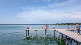 Sitzende und schwimmende Menschen am Badesteg des Ammersee in Hersching