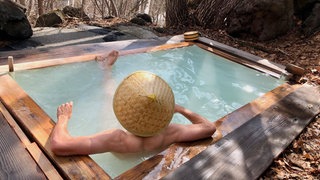 Mann mit japanischem Hut badet in einem Onsen, Japan