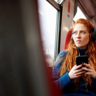 Eine Frau mit Kopfhörern während einer Bahnfahrt 