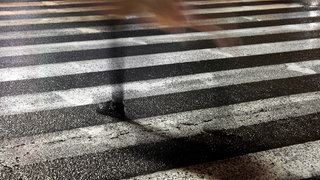 Symbolbild. Eine junge Frau verschwindet beim Überqueren der nassen Straße in der Nacht
