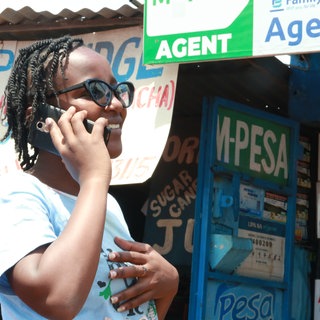 Eine Frau mit Handy am Ohr steht vor einem M-Pesa-Kiosk: Überall in Afrika zahlen Menschen per Smartphone-App. Auch Geldtransfers und andere Finanzgeschäfte werden digital erledigt. Dadurch sind Kleinhändler oder Bauern, die kein Bankkonto haben, nicht länger vom internationalen Wirtschaftssystem ausgeschlossen. Manche in Afrika entwickelte Technik wird inzwischen weltweit genutzt. 