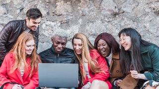 Studentengruppe sitzt vor einem Laptop: Während des Studiums gibt es viele Möglichkeiten, in eine andere Kultur zu schnuppern, Sprachen zu lernen, andere Hochschulsysteme kennenzulernen. Seit 35 Jahren gibt es das Erasmus-Programm. Doch der Bologna-Prozess, der Brexit und die Pandemie schaffen neue Hürden. 