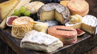 Verschiedene Käsesorten auf einem Holzbrett: Viele Leute schneiden die Rinde beim Käse weg, das wäre aber in den meisten Fällen zumindest aus gesundheitlichen Gründen nicht nötig.
