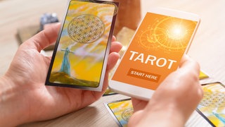 Tarotkarten und Smartphone mit Wahrsage-App: Auf Social Media bieten spirituelle Coaches Instagram-Lives zu Yoga und Meditation an, posten Kacheln zu Selbstliebe und positivem Denken oder legen Tarot-Karten. 