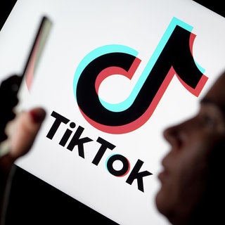Silhouette einer Frau, die ein Smartphone hält, im Hintergrund das Logo der Videoplattform TikTok: Die Social-Media-Plattform TikTok ist schon lange Teil der Popkultur – mittlerweile zeigt sich aber auch der politische Einfluss der App. Denn neben Influencern tummeln sich hier auch Parteien, Politiker und Aktivisten.