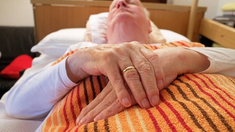 Ein alter Mann liegt im Bett: Wenn die Schmerzen unerträglich werden und keine Aussicht auf Besserung besteht, entscheiden sich manche Menschen dafür, auf Essen und Trinken zu verzichten. Das "Sterbefasten" gilt als eine eher natürliche Form des Sterbens, da Sterbende in ihrer letzten Lebensphase ohnehin weniger bzw. gar keine Nahrung mehr zu sich nehmen.