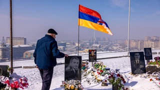 Der 28. Januar ist in Armenien der "Tag der Armee". Auf dem Soldatenfriedhof Jerablur in der Hauptstadt Jerewan besucht 2024 ein Mann an diesem Tag ein blumengeschmücktes Grab und berüht das Bild eines Gefallenen. Daneben weht die Flagge von Bergkarabach. Auf dem Friedhof wurden Soldaten beerdigt, die im Konflikt zwischen Armenien und Aserbaidschan um Bergkarabach starben.