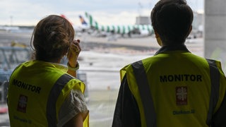 Finn Dohrmann (rechts) und Melisa Ergül-Puopolo stehen im Terminal 1 des Frankfurter Flughafens an einer Fensterscheibe mit Blick auf das Vorfeld. Sie sind als Abschiebebeobachter in kirchlichem Auftrag am Flughafen bei vielen dieser Rückführungen dabei. Ihre Aufgabe ist es, "Verstöße gegen die Verhältnismäßigkeit von eingesetzten Mittel und Verletzungen humanitärer Ansprüche" zu dokumentieren. 