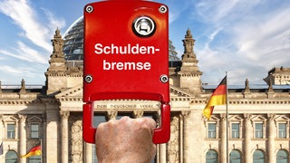 Eine Hand zieht an einer roten "Schuldenbremse" vor dem Berliner Reichstag (Symbolfoto): Die Schuldenbremse gibt vor, dass die Regierung maximal 0,35 Prozent des Bruttoinlandsproduktes an Nettoneukrediten aufnehmen darf. Kritiker finden, dass die Schuldenbremse dringend nötige Investitionen verhindert. Befürworter warnen, dass eine Lockerung Regierungen dazu verführen würde, zu viel Geld auf Pump auszugeben, weil sie an der Macht bleiben wollen. 