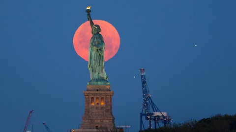 Besonders tiefer Erdbeermond über der Freiheitsstatue in New York.
