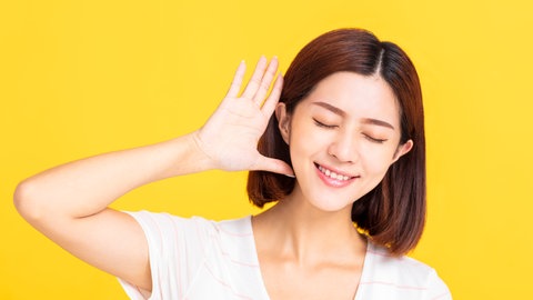 Junge Frau hält sich lauschend eine Hand hinter das Ohr: Absolutes Gehör bedeutet, dass ich zu jemandem sagen kann "Sing mal ein G!" – und die Person trifft dann genau den richtigen Ton. Das ist eine besondere musikalische Gabe. 