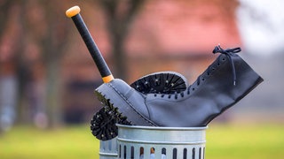 Springerstiefel und Baseballschläger im Abfalleimer als Symbolbild für den Ausstieg aus der rechten Szene: Extremisten einen Ausstieg aus ihrer Szene zu ermöglichen, ist aufwendig, der Erfolg vieler Ausstiegsprogramme ungewiss