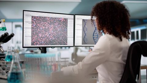 Junge Wissenschaftlerin in einem Labor vor Computerbildschirmen: Viele Wissenschaftlerinnen und Wissenschaftler in den USA spielen mit dem Gedanken auszuwandern, und deutsche Organisationen preisen den Wissenschaftsstandort Deutschland als Alternative an.