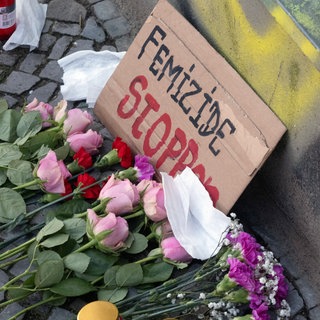 Blumen, niedergelegt für das Opfer eines Femizids. Auf einem Schild steht: "Femizide stoppen". Jedes Jahr versuchen in Deutschland geschätzt hunderte Männer ihre Partnerinnen und Ex-Partnerinnen zu ermorden, fast jeden zweiten Tag stirbt eine Frau.