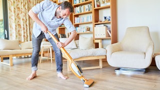 Ein Mann saugt barfuß das Wohnzimmer: Sterben Spinnen, wenn man sie mit dem Staubsauger aufsaugt?