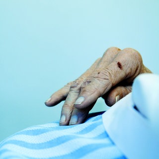 Hand eines alten Menschen auf einer Bettdecke: Selten kommt der Tod plötzlich. Er braucht Zeit. Die einen sterben schneller, die anderen langsamer. Wie unterscheiden sich klinischer Tod und Hirntod? Und wachsen Haare auch nach dem Tod noch weiter? 