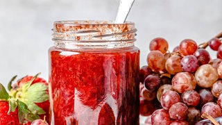 Marmeladenglas mit Löffel, drum herum Früchte: Verhindert ein Silberlöffel beim Marmeladeeinfüllen das Zerspringen des Glases?