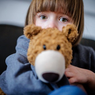 Verängstigtes Kind klammert sich an Teddybär: Viele Kinder entwickeln Ängste: vor Hunden, der Dunkelheit, der Schule oder der Trennung von den Eltern. Oft verschwinden die Ängste von selbst, doch manchmal bleiben sie und schränken das Leben ein. 