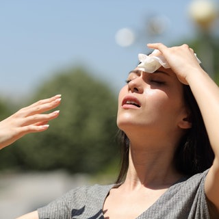 Symbolbild: Eine Frau trocknet an einem warmen Sommertag Schweiß mit einem Tuch ab.