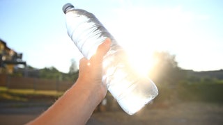 Eine Hand hält eine Wasserflasche: Kann man Wasser durch Schütteln zum Kochen bringen?