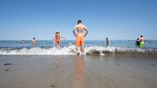 Menschen stehen im Wasser am Ostseestrand in Kühlungsborn.