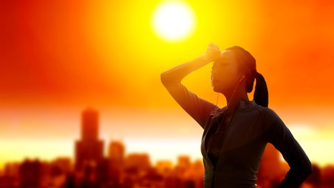 Eine Frau schützt in heißer Sonne ihre Augen: Hitzewellen sind belastend, doch mit der richtigen Anpassung lassen sie sich gut überstehen. Dazu gehört, sich nicht nur in klimatisierten Räumen zu schonen, sondern den Körper an Hitze zu gewöhnen.
