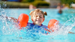 Kleines Mädchen mit Schwimmflügeln planscht im Pool: In den letzten Jahren steigt die Zahl der Grundschüler, die nicht schwimmen können. Die Gründe sind vielfältig.