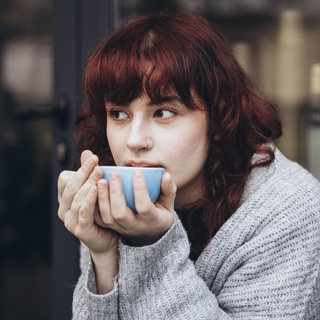 Junge Frau trinkt aus einer Tasse: Sind Tee und Kaffee Kalziumräuber und schlecht für die Knochen?