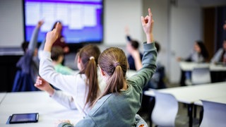 Schülerinnen und Schüler einer siebten Klasse melden sich in einem Klassenraum.
