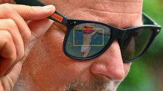 Fotomontage; Symbolfoto: Smartglasses fangen heimlich eine Frau im Bikini am Strand ein.