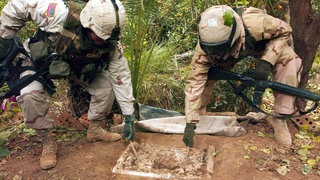 Zwei US-Soldaten der 1. Brigade der 4. Infanteriedivision heben die Schaumstoffabdeckung auf das Erdloch, in dem sich der ehemalige irakische Führer Saddam Hussein versteckt gehalten hatte. Spezialeinheiten nahmen Hussein am 15. Dezembr 2003 hier fest.