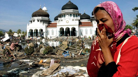 Eine Frau bedeckt ihre Nase mit einem Tuch; im Hintergrund eine Moschee. In den Straßen ist der Müll zu sehen, der sich nach dem Erdbeben und Tsunami in Banda Aceh auf der indonesischen Insel Sumatra im Dezember 2004 angesammelt hat.
