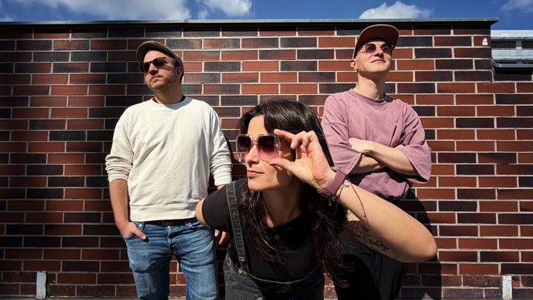 Das Trio "freezy bakery" steht vor einer Backsteinwand. 