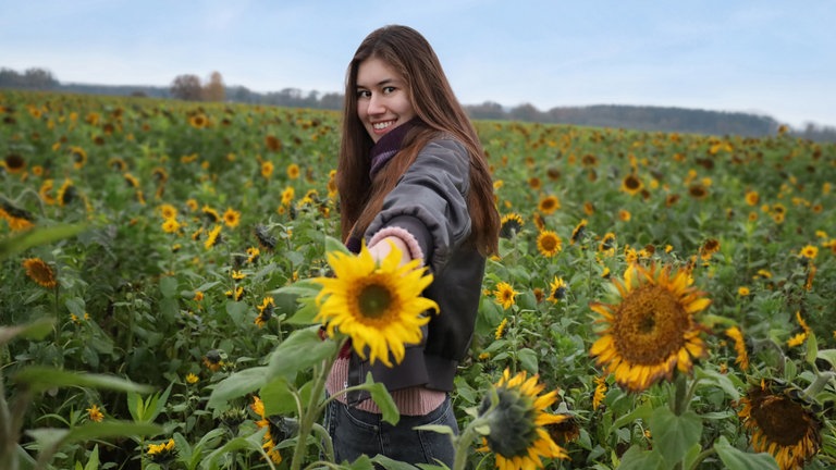 Die Ulmer Songwriterin und Gitarristin Anica Wondra steht in einem Sonnenblumenfeld und hält eine Sonnenblume in der Hand