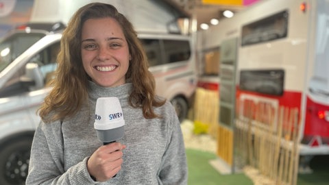 SWR Volontärin Jara Nagi steht mit einem Mikrofon vor einem Campervan