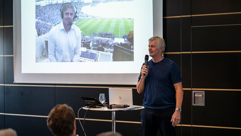 ARDSWR Sportkommentator Tom Bartels zeigt den Kommentator-Platz im Stadion.