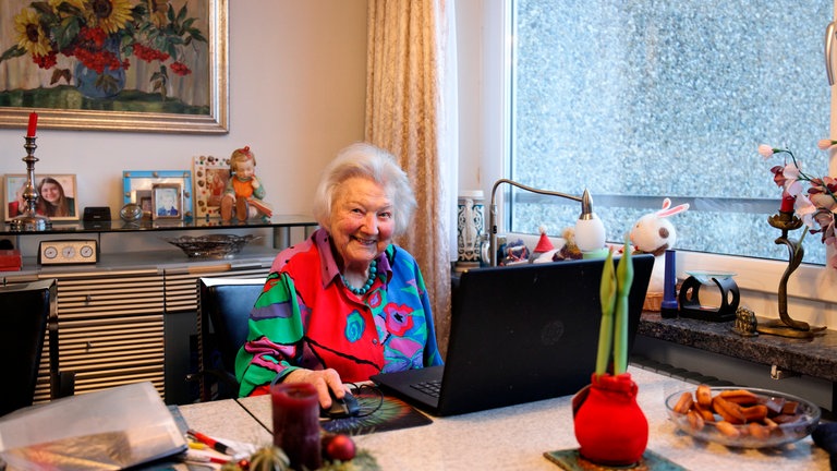 Hildegard am Schreibtisch vor einem Laptop, sie ist 98 Jahre alt und investiert seit über 50 Jahren Geld in Aktien.