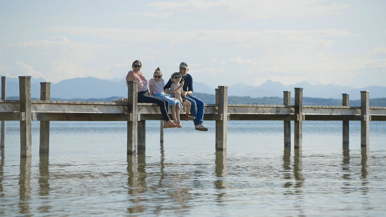 Die Familie sitzt auf einem Steg im Sommer, lassen die Beine baumeln über dem Wasser