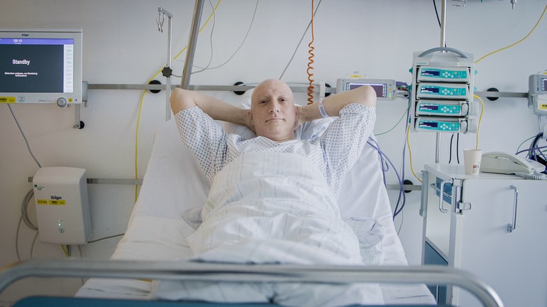 Philipp liegt im Krankenhausbett, neben ihm viele Gräte, die Arme hinter dem Kopf verschränkt, blickt in die Kamera