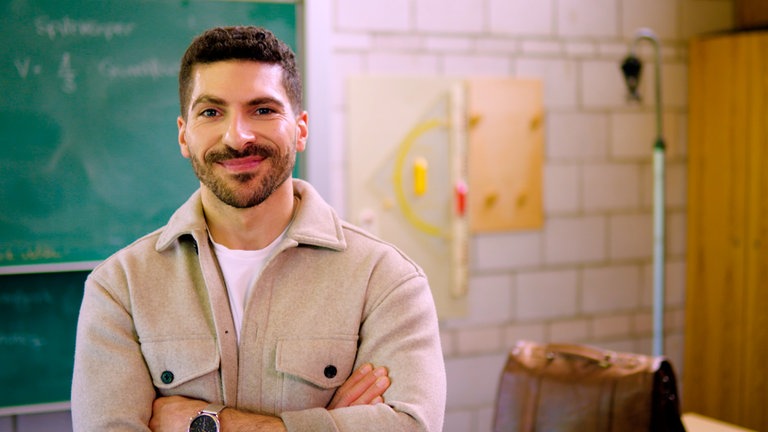 Resul ist Lehrer und steht in einem Klassenzimmer vor einer grünen Tafel. Resul macht mit bei "SWR Heimat. Der Ort für deine Geschichte."