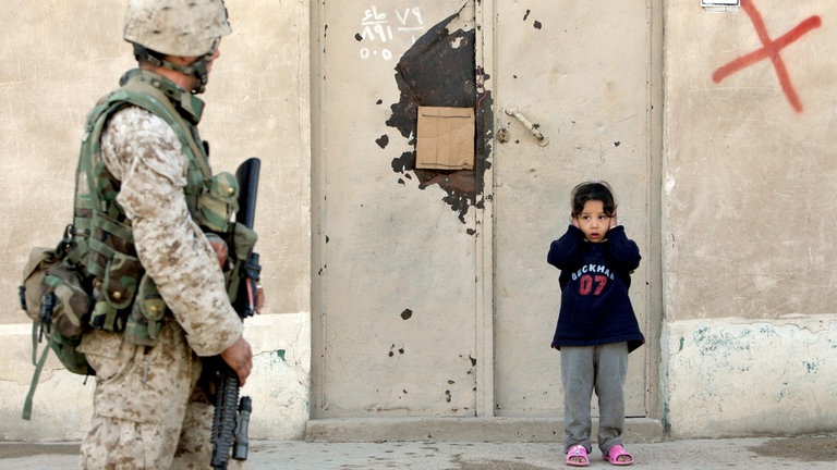 Falludscha, Irak, 2005: Ein irakisches Mädchen hält sich die Ohren zu, als ein Marine der Ersten Division im Zentrum der schwer bewachten Stadt Falludscha patrouilliert.