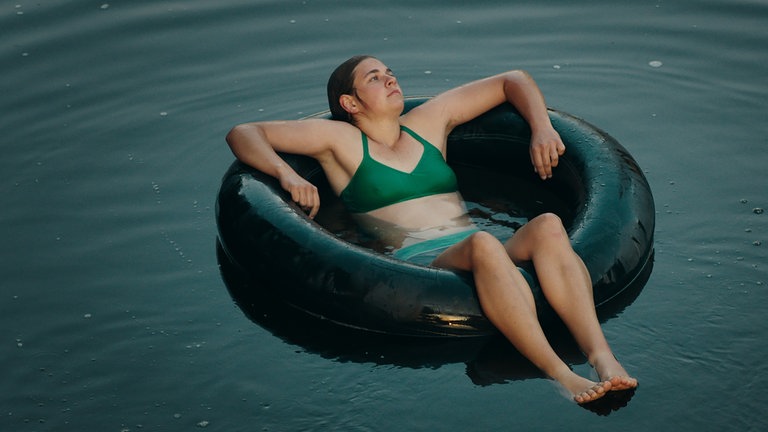 Katinka (Karolin Nothacke) in einem grünen Bikini lässt sich in einem großen Schwimmring auf dem See treiben.