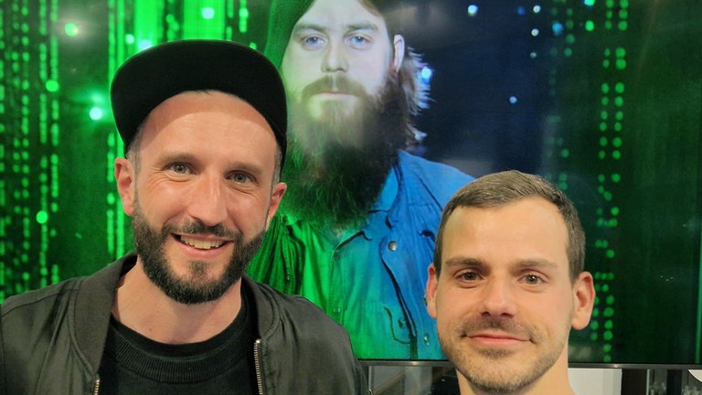 Die Regisseure Benjamin Rost (li.) und Erec Brehmer (re.) vor einer Videowand mit dem Portrait von Filmfälscher Michael Born